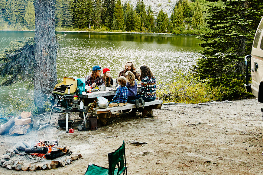 A family camping having lunch on a picnic table by the lake