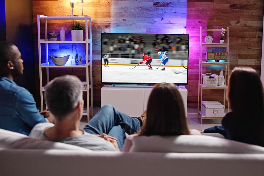 A group of friends sitting on a coach and watching a game of hockey on TV