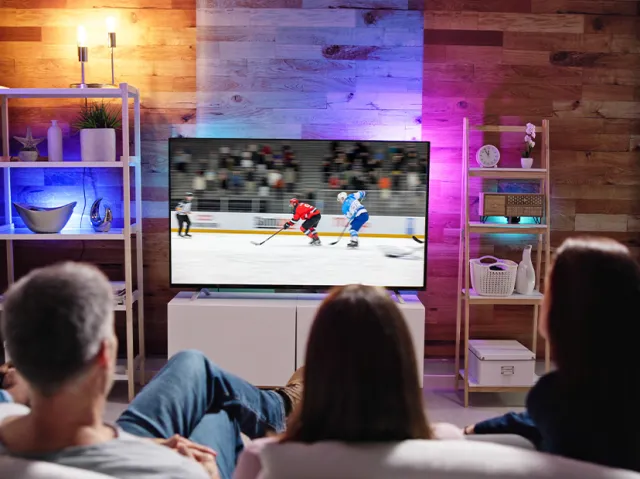 A group of friends sitting on a coach and watching a game of hockey on TV