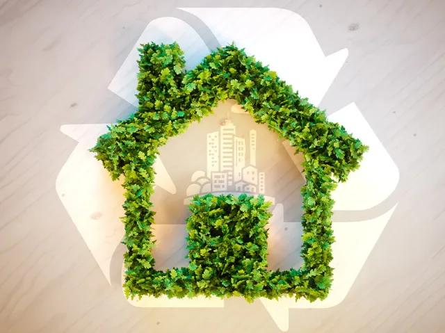 A house shaped in green leaves with a recycle logo in the background