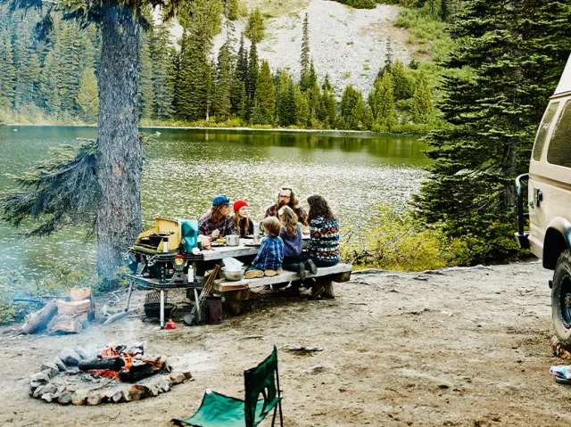 A family camping having lunch on a picnic table by the lake