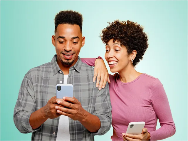 Un homme et une femme sourient en regardant un téléphone intelligent. 